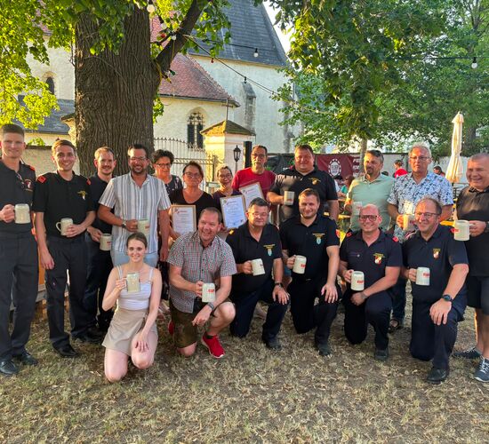 Gruppe von Menschen feiert mit Bierkrügen unter Bäumen, lächelnd und posierend für das Foto.