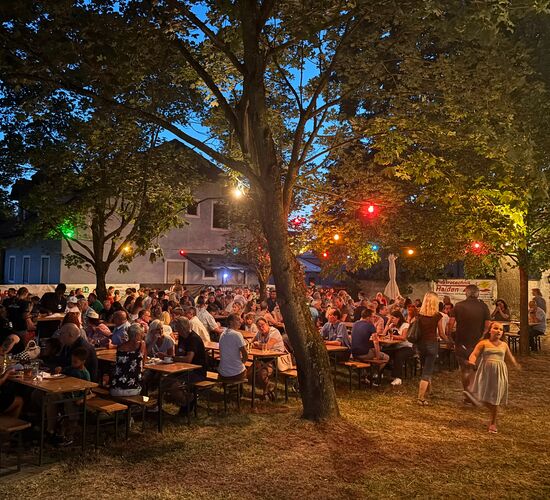 Eine lebhafte Sommernacht mit vielen Menschen, die an Tischen unter bunten Lichtern feiern.